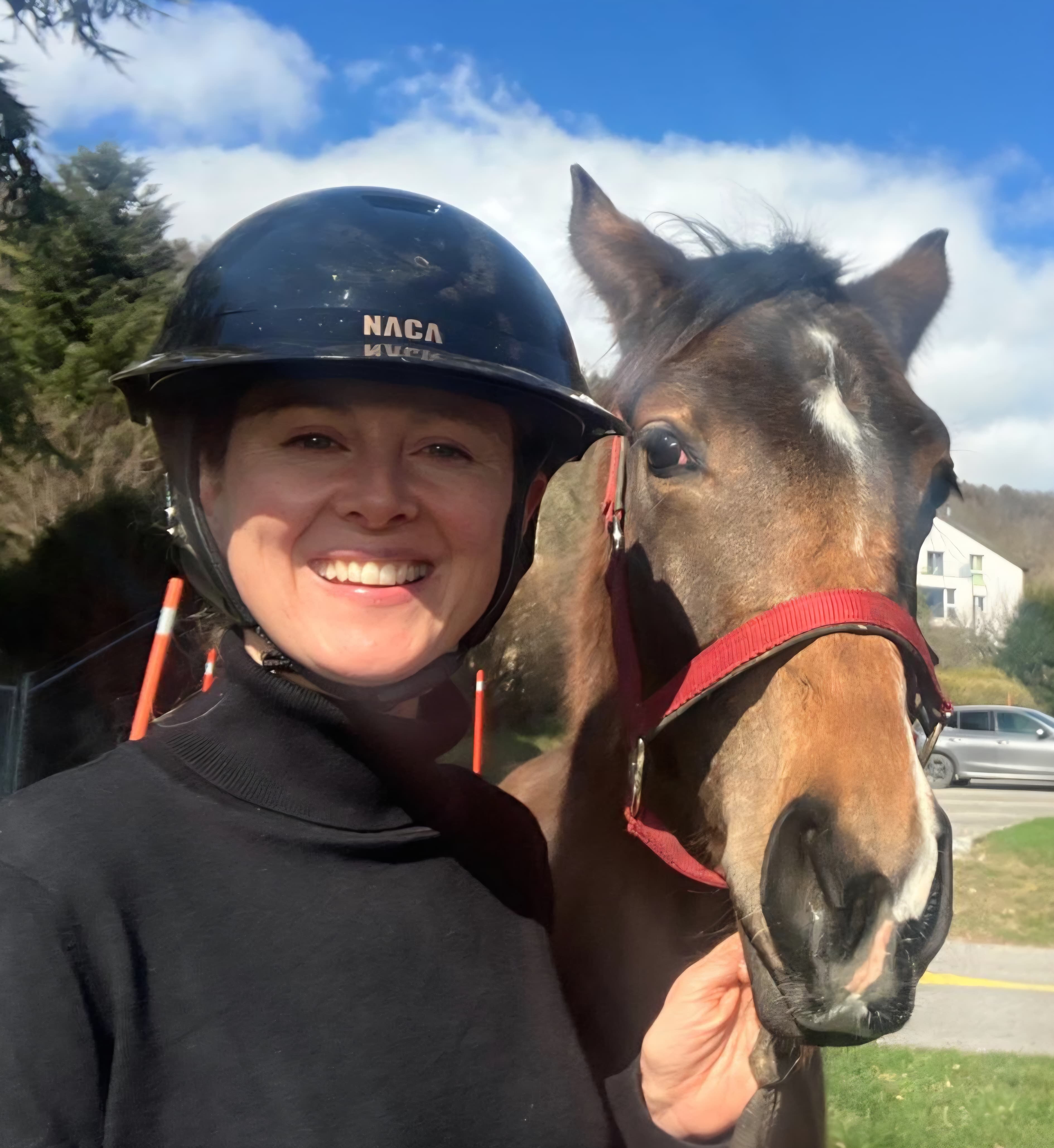 Une cavalière portant une bombe noire, jugulaire attachée, sur un cheval alezan dans un manège couvert